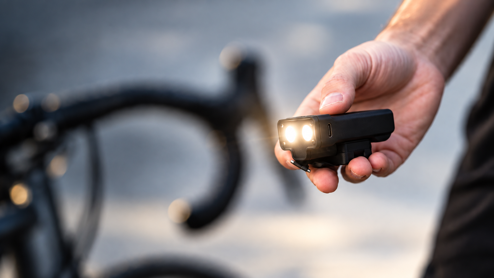 Hand hält das leuchtende KEEP·IT Fahrradlicht vor einem Gravelbike-Lenker